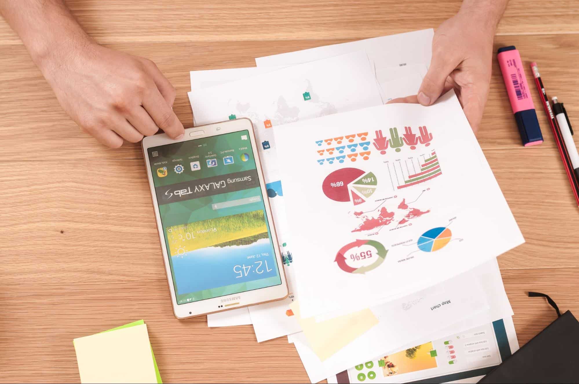 A tablet and papers with pie charts on a desk.