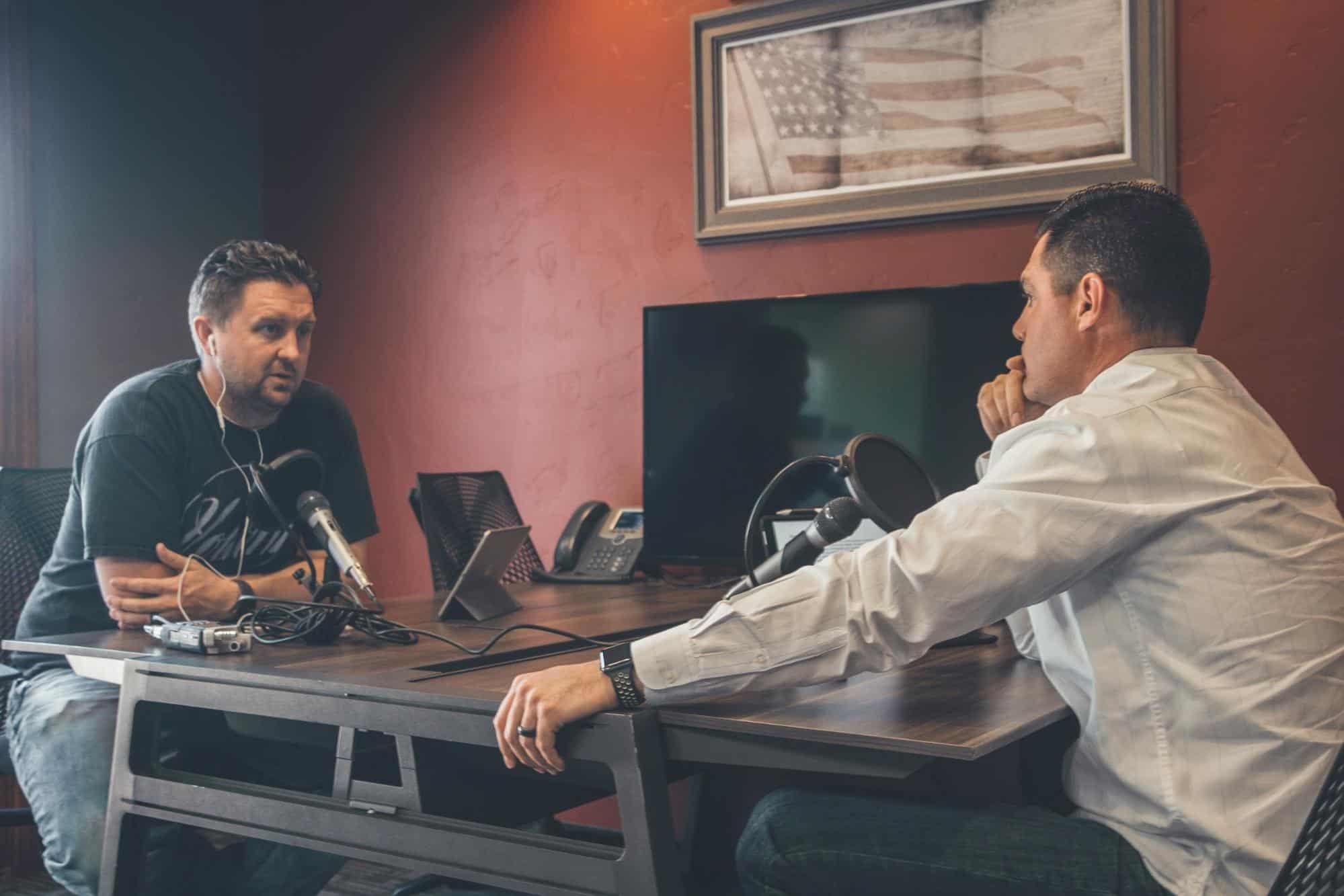 Two businessmen engaging in conversation at a desk, potentially discussing business blog strategies or content marketing tactics.