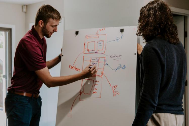Two people drawing on a whiteboard.