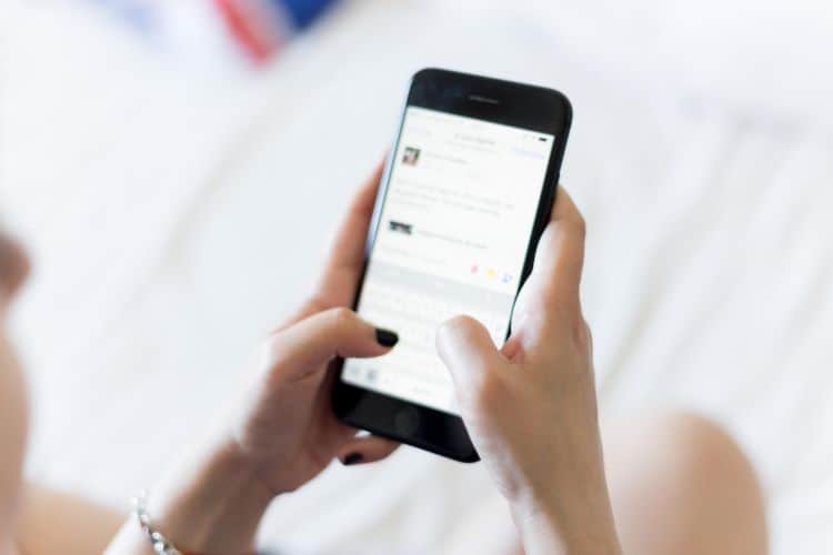A woman is using a smart phone on a bed.