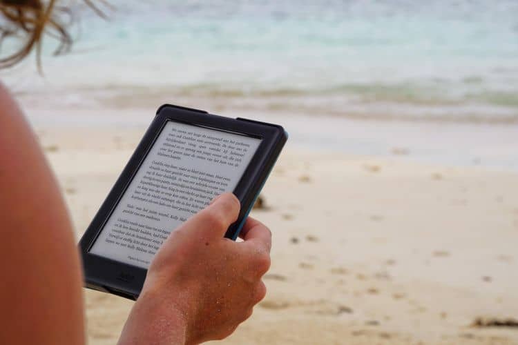 A woman holds an electronic reader on the sand.