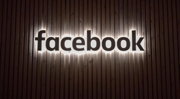 The facebook logo is lit up on a wooden wall.