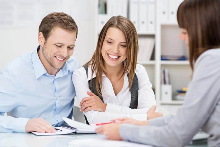 saleswoman-talking-to-clients A man and a woman sitting at a desk with papers.