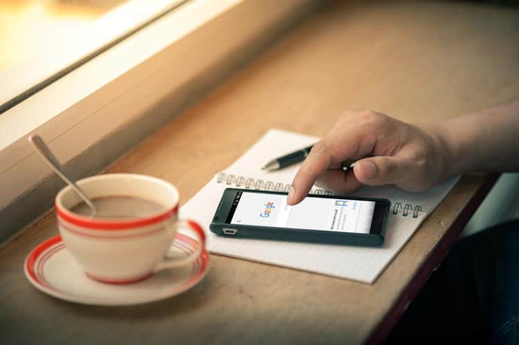 A person using a smartphone on a table next to a cup of coffee.