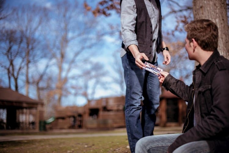 A man giving a card to another man in a park.