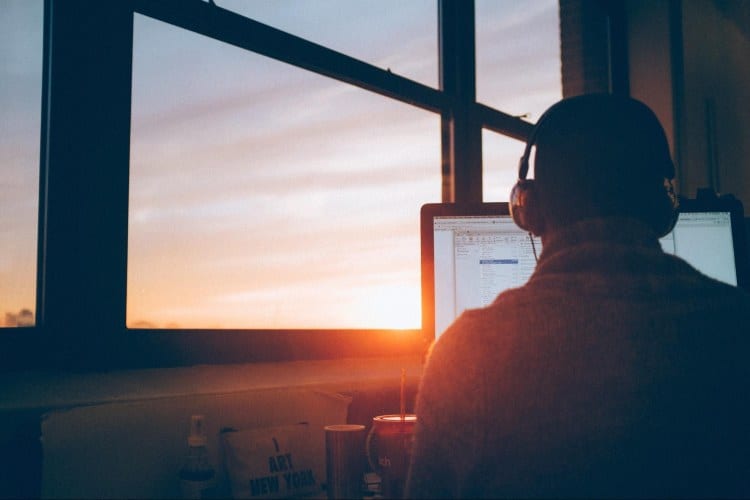 A person sitting in front of a window working on a computer.