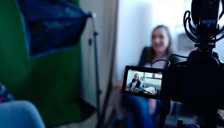 A woman is sitting in front of a video camera.