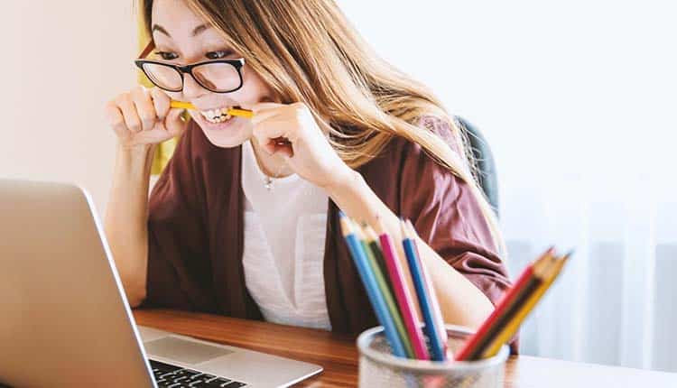 A woman wearing glasses is sitting at a desk with a laptop and pencils.