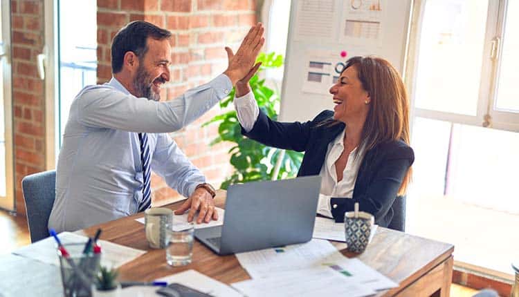 Two business people giving each other high fives in an office.