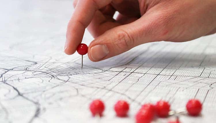 A hand pointing to a map with red pins.