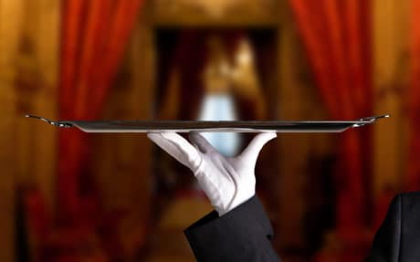 A waiter holding a tray in front of a red curtain.