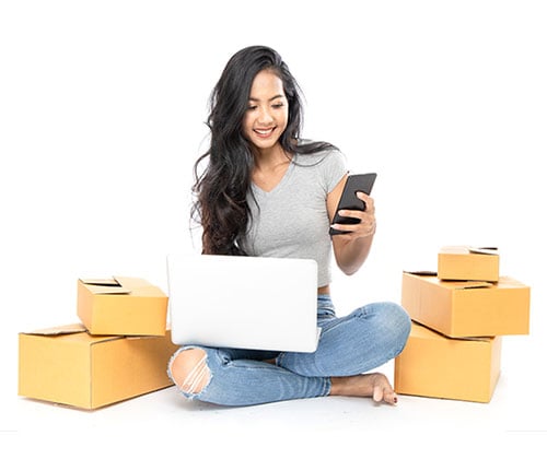 A woman sitting on the ground with a laptop and boxes.