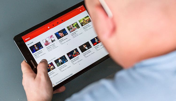 A person from behind viewing a youtube homepage on a tablet, touching the screen to select a video.