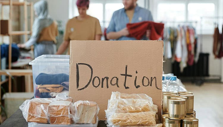 People are organizing donated items including clothes, canned goods, and packaged food. A cardboard sign in the center reads "Donation.