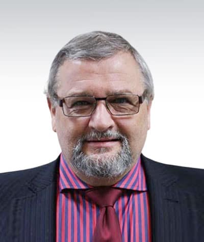 adrian-griffin-5 A man with graying hair and glasses, wearing a dark suit, a red striped shirt, and a red tie, smiles at the camera against a plain background.