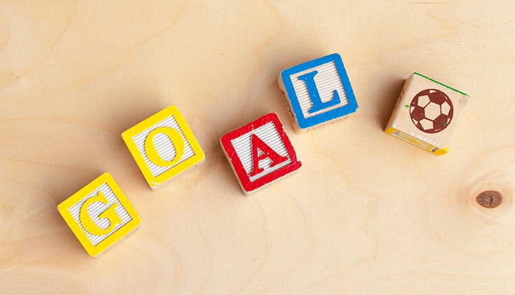 Wooden blocks spelling "GOAL" with a soccer ball image on one block, arranged diagonally on a wooden surface.