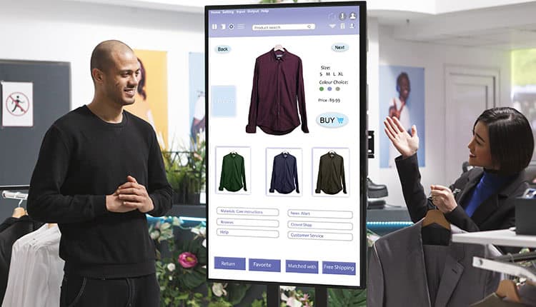 A man and a woman stand near a digital display showing shirt options, including size, color, and purchase details, in a modern clothing store.