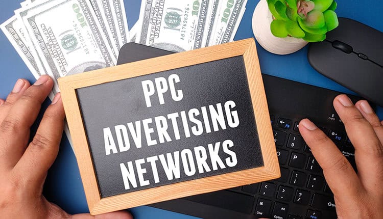 A person holds a small chalkboard with the text "PPC Advertising Networks" 
