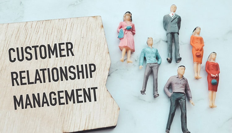A wooden block with the words "Customer Relationship Management" next to six miniature figurines of people on a light surface.