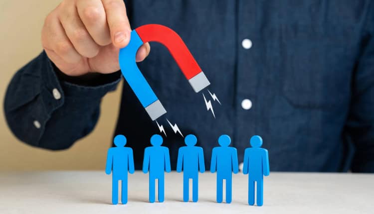 A person holds a red and blue magnet above five blue human-shaped figures